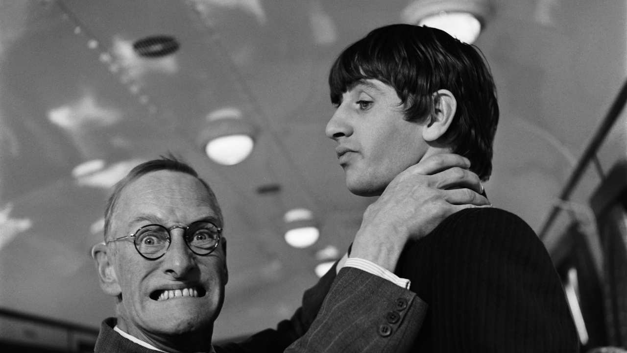 a mn with glasses pretending to choke Ringo Starr